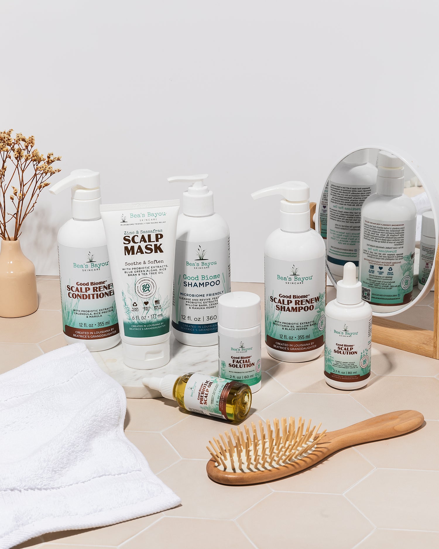 Three skincare products with droppers on a teal background, surrounded by green leaves. bottles labeled &quot;bayou&quot; include scalp solution and prebiotic serum.